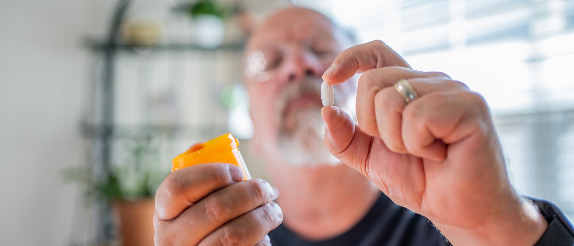 Älterer Mann begutachtet skeptisch eine Pille in seiner linken Hand und hält in der rechten eine Pillendose.
