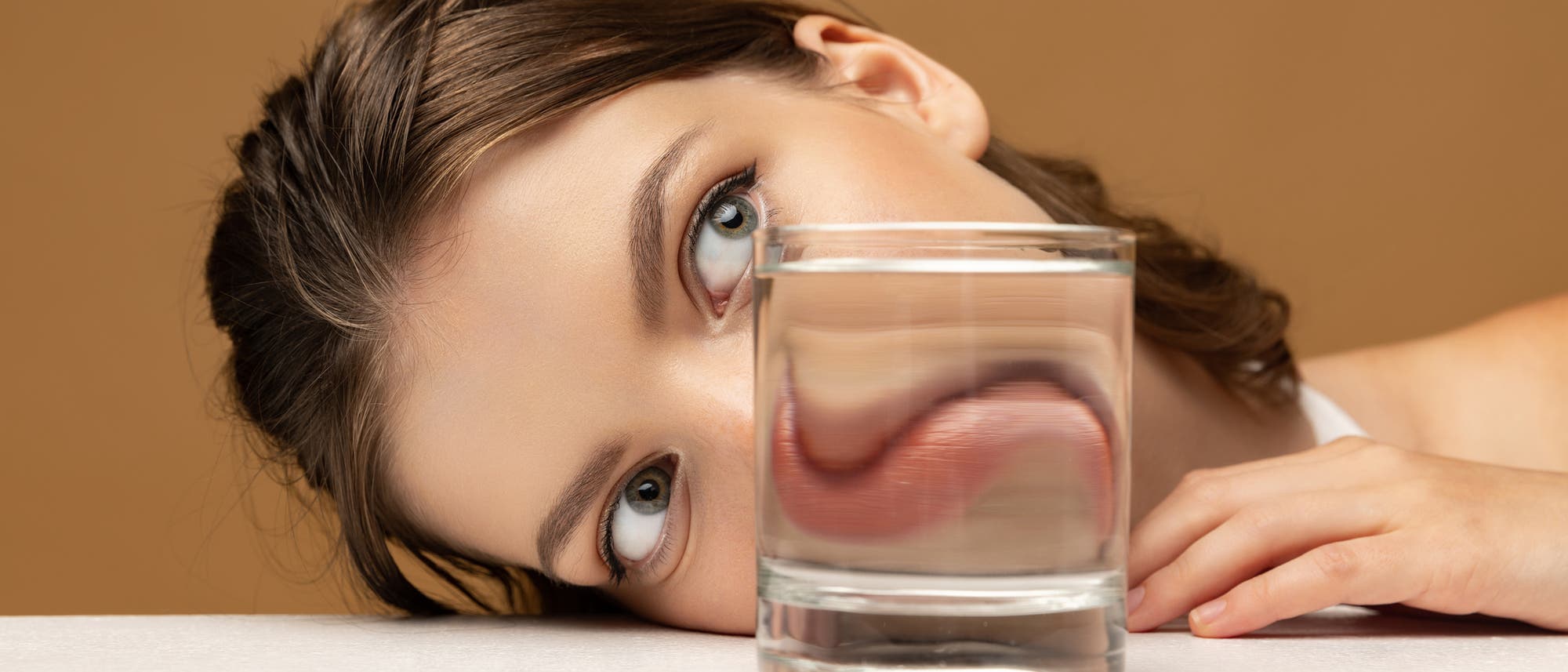 Gesicht einer jungen Frau, deren Mund hinter einem Glas verzerrt erscheint 