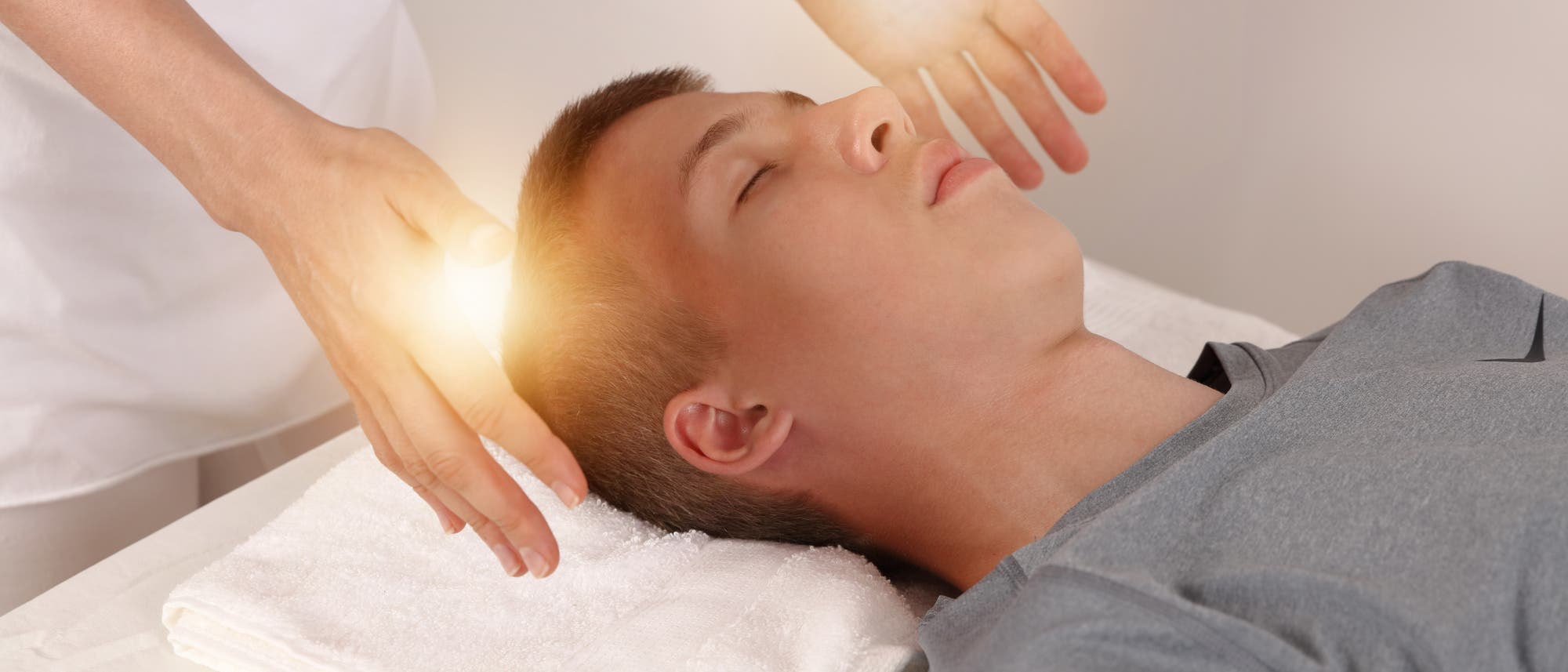 Eine Person liegt entspannt auf einem Tisch mit einem Handtuch unter dem Kopf. Zwei Hände schweben über dem Kopf der Person, umgeben von einem sanften Lichtschein, was auf eine energetische oder therapeutische Behandlung hindeutet. Die Szene vermittelt Ruhe und Entspannung. Eine Person liegt entspannt auf einem Tisch mit einem Handtuch unter dem Kopf. Zwei Hände schweben über dem Kopf der Person, umgeben von einem sanften Lichtschein, was auf eine energetische oder therapeutische Behandlung hindeutet. Die Szene vermittelt Ruhe und Entspannung.
