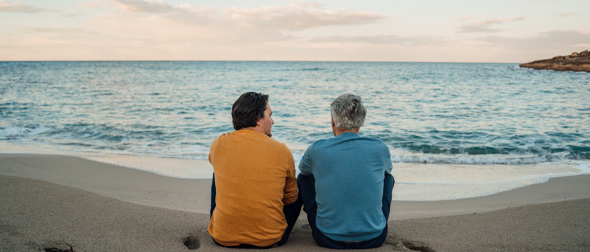 Zwei Personen sitzen am Strand und blicken auf das Meer. Der Himmel ist leicht bewölkt, und die Wellen rollen sanft an den Sand. Die Personen tragen Freizeitkleidung und scheinen in ein Gespräch vertieft zu sein. Die Szene vermittelt eine ruhige und entspannte Atmosphäre. Zwei Personen sitzen am Strand und blicken auf das Meer. Der Himmel ist leicht bewölkt, und die Wellen rollen sanft an den Sand. Die Personen tragen Freizeitkleidung und scheinen in ein Gespräch vertieft zu sein. Die Szene vermittelt eine ruhige und entspannte Atmosphäre.