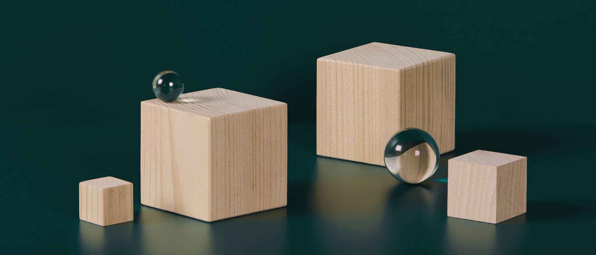 Eine 3D-Darstellung zeigt vier unterschiedlich große Holzwürfel auf einer dunklen Oberfläche. Zwei transparente Kugeln liegen auf den Würfeln, eine auf dem größten und eine auf dem zweitgrößten Würfel. Die Szene ist minimalistisch und hebt die geometrischen Formen und Materialien hervor. Eine 3D-Darstellung zeigt vier unterschiedlich große Holzwürfel auf einer dunklen Oberfläche. Zwei transparente Kugeln liegen auf den Würfeln, eine auf dem größten und eine auf dem zweitgrößten Würfel. Die Szene ist minimalistisch und hebt die geometrischen Formen und Materialien hervor.
