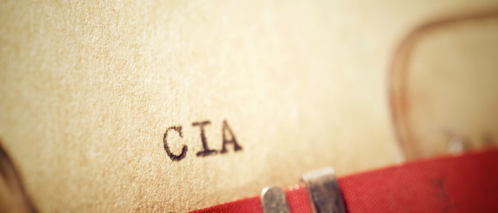 Eine Nahaufnahme einer Schreibmaschine, die das Wort "CIA" auf ein beiges Blatt Papier tippt. Der Fokus liegt auf den getippten Buchstaben, w&auml;hrend der Rest des Bildes leicht verschwommen ist. Die Szene vermittelt ein Gef&uuml;hl von Geheimhaltung und klassischer B&uuml;roarbeit.
