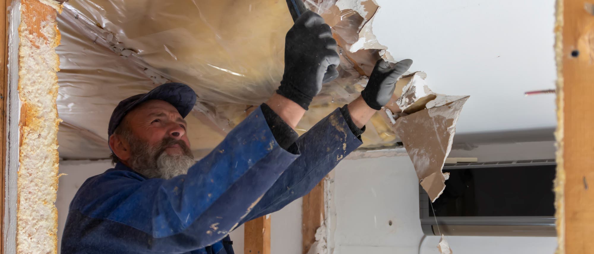 Ein Arbeiter entfernt ohne Mundschutz die Deckenverkleidung in einem Haus