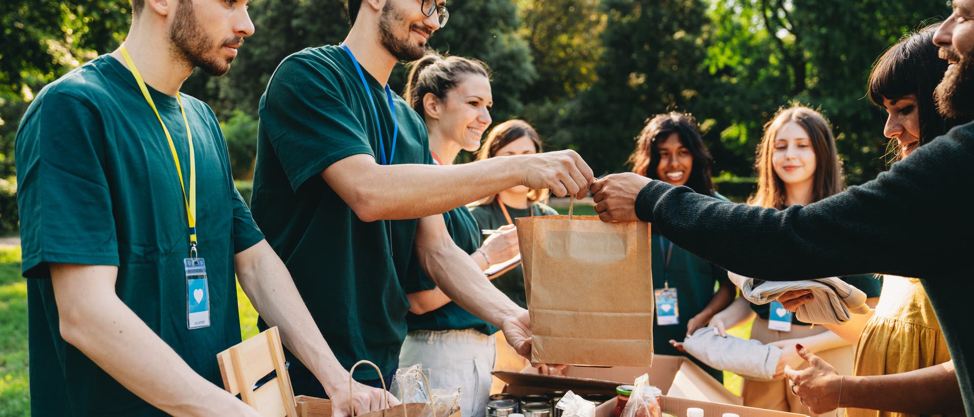Ein junger Mann gibt einem Pärchen an der Lebensmitteltafel lächelnd eine Tüte mit Lebensmitteln. 