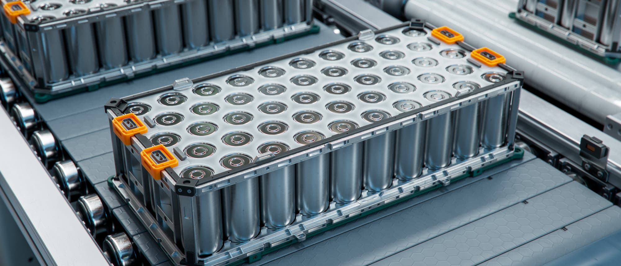 Eine Nahaufnahme eines Batteriepakets auf einem Förderband in einer Fabrik. Die Batterien sind in einem rechteckigen Metallgehäuse angeordnet, mit orangefarbenen Griffen an den Ecken. Das Bild zeigt den industriellen Herstellungsprozess von Batterien, möglicherweise für Elektrofahrzeuge oder Energiespeicherlösungen. Keine Menschen sind im Bild zu sehen. Eine Nahaufnahme eines Batteriepakets auf einem Förderband in einer Fabrik. Die Batterien sind in einem rechteckigen Metallgehäuse angeordnet, mit orangefarbenen Griffen an den Ecken. Das Bild zeigt den industriellen Herstellungsprozess von Batterien, möglicherweise für Elektrofahrzeuge oder Energiespeicherlösungen. Keine Menschen sind im Bild zu sehen.