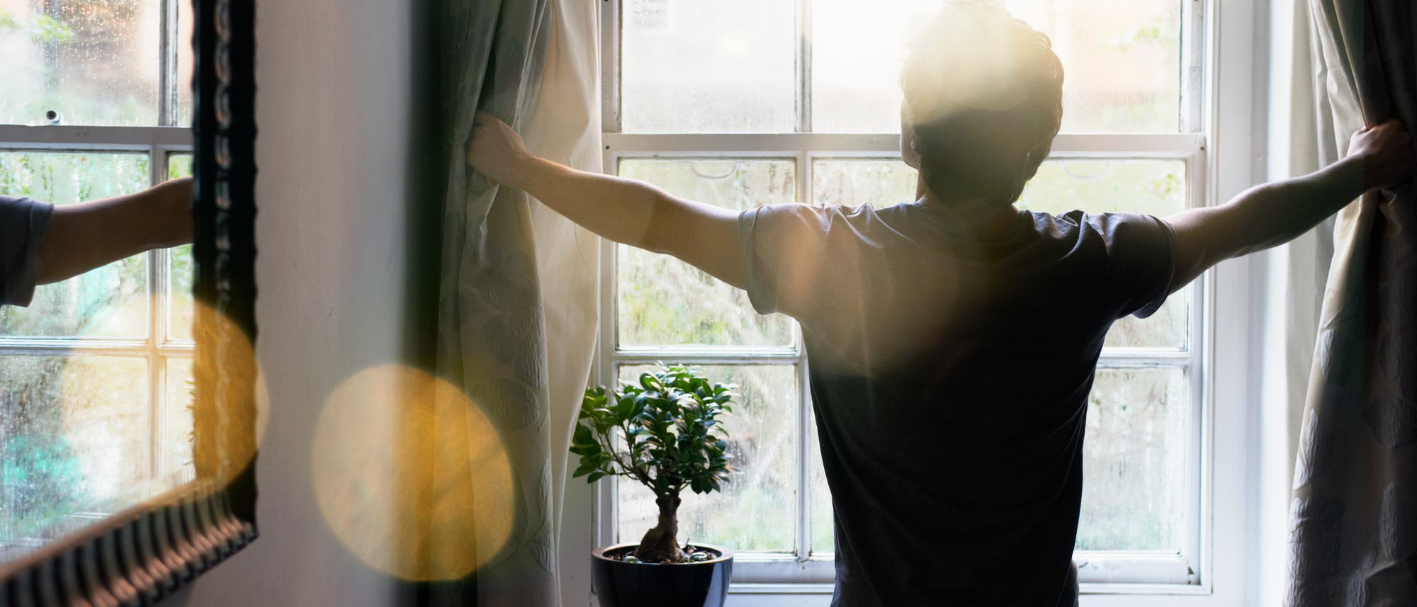 Eine Person steht mit dem Rücken zur Kamera und zieht die Vorhänge eines großen Fensters auf, durch das Sonnenlicht hereinfällt. Auf der Fensterbank steht eine kleine Topfpflanze. Die Szene wirkt ruhig und einladend, mit einem Fokus auf Morgenlicht und Natur. Eine Person steht mit dem Rücken zur Kamera und zieht die Vorhänge eines großen Fensters auf, durch das Sonnenlicht hereinfällt. Auf der Fensterbank steht eine kleine Topfpflanze. Die Szene wirkt ruhig und einladend, mit einem Fokus auf Morgenlicht und Natur.