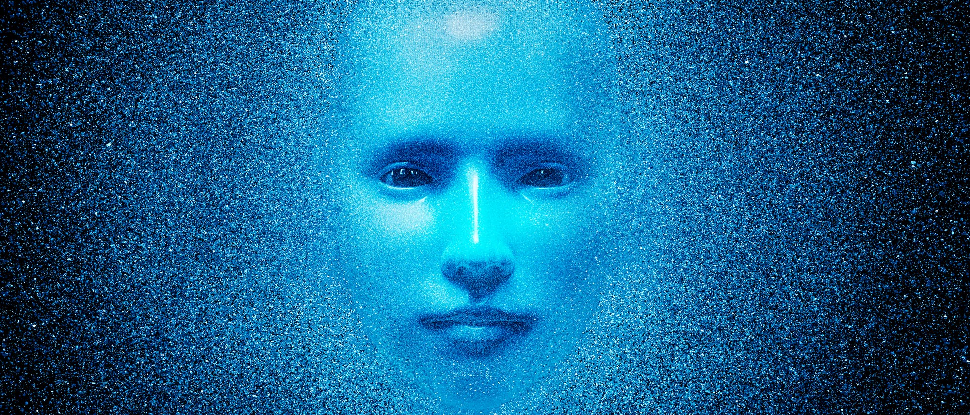 Ein digitales Kunstwerk zeigt ein blaues, stilisiertes Gesicht, das aus einem Hintergrund aus feinen, glitzernden Partikeln hervorzutreten scheint. Die Gesichtszüge sind weich und abstrahiert, was dem Bild eine futuristische und mystische Atmosphäre verleiht. Der Hintergrund ist dunkelblau und verstärkt den leuchtenden Effekt des Gesichts. Das Bild vermittelt ein Gefühl von Technologie und Unendlichkeit.