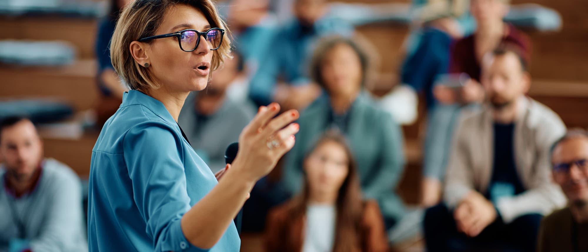 Eine Hochschullehrerin mit Mikrofon steht vor Studierenden in einem Hörsaal