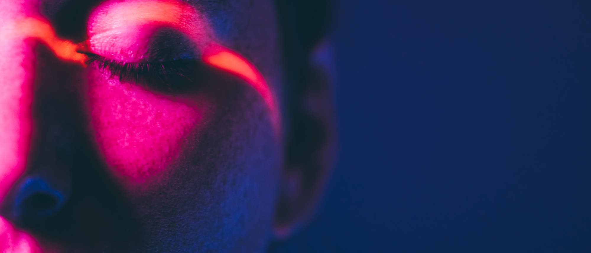 Nahaufnahme eines Gesichts mit geschlossenen Augen, beleuchtet von intensivem pinkem und blauem Licht. Ein roter Lichtstreifen verläuft diagonal über das Auge. Die Szene wirkt künstlerisch und futuristisch. Keine Text- oder URL-Informationen vorhanden. Nahaufnahme eines Gesichts mit geschlossenen Augen, beleuchtet von intensivem pinkem und blauem Licht. Ein roter Lichtstreifen verläuft diagonal über das Auge. Die Szene wirkt künstlerisch und futuristisch. Keine Text- oder URL-Informationen vorhanden.