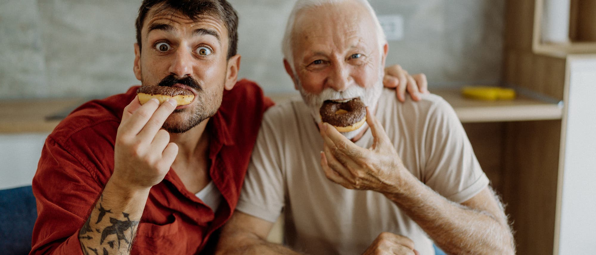 Ein junger und ein alter Mann essen Donuts.