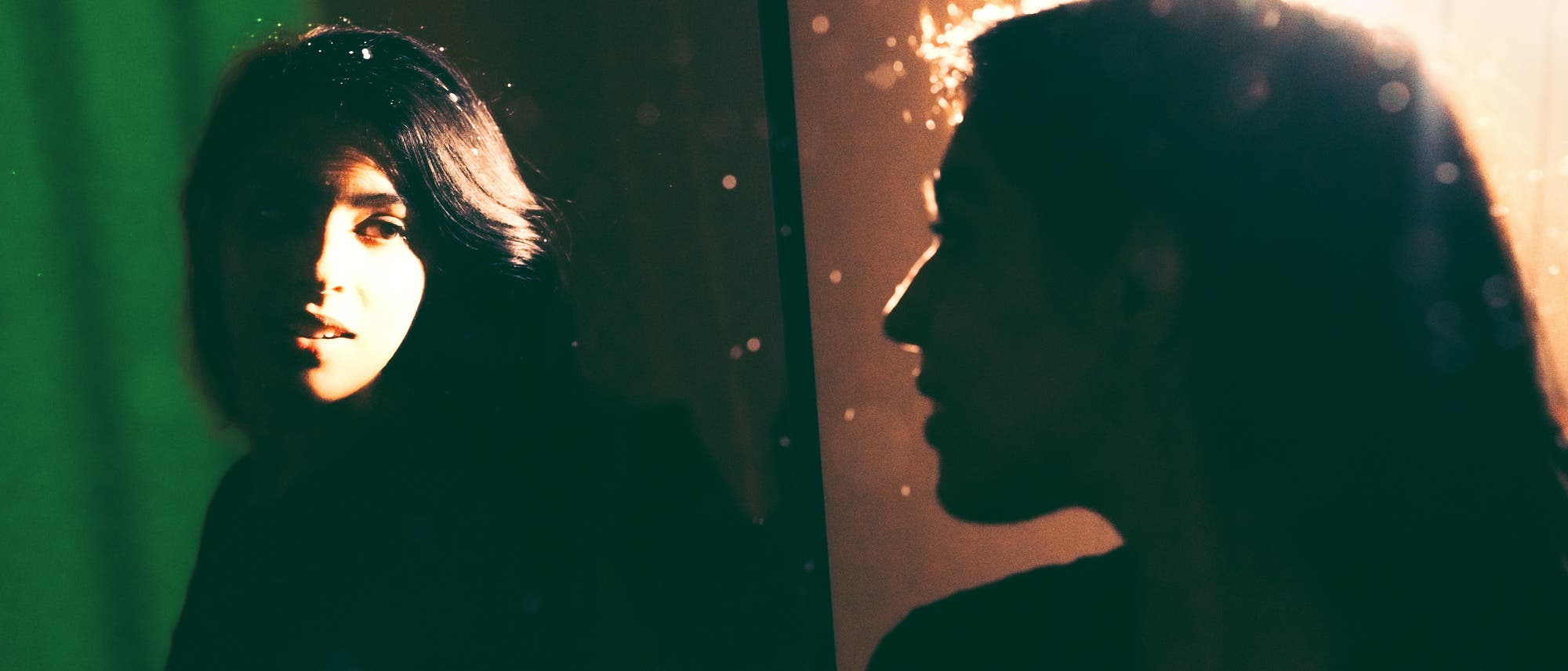 Eine Person steht vor einem Spiegel, der ihr Gesicht reflektiert. Die Szene ist in warmes, ged&auml;mpftes Licht getaucht, das von der rechten Seite kommt und einen Kontrast zwischen Licht und Schatten erzeugt. Staubpartikel sind im Licht sichtbar, was der Aufnahme eine atmosph&auml;rische Tiefe verleiht. Der Hintergrund ist unscharf und in dunklen T&ouml;nen gehalten.