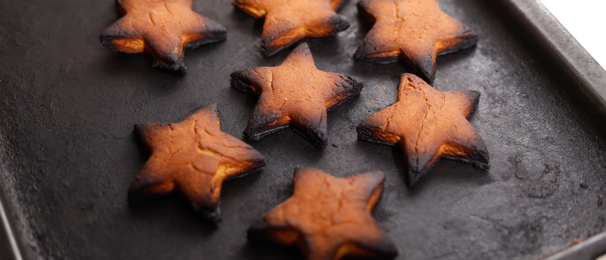 Foto von an den Ecken verbrannten sternförmigen Weihnachtsplätzchen, die auf einem Blech aus dem Backofen geholt werden