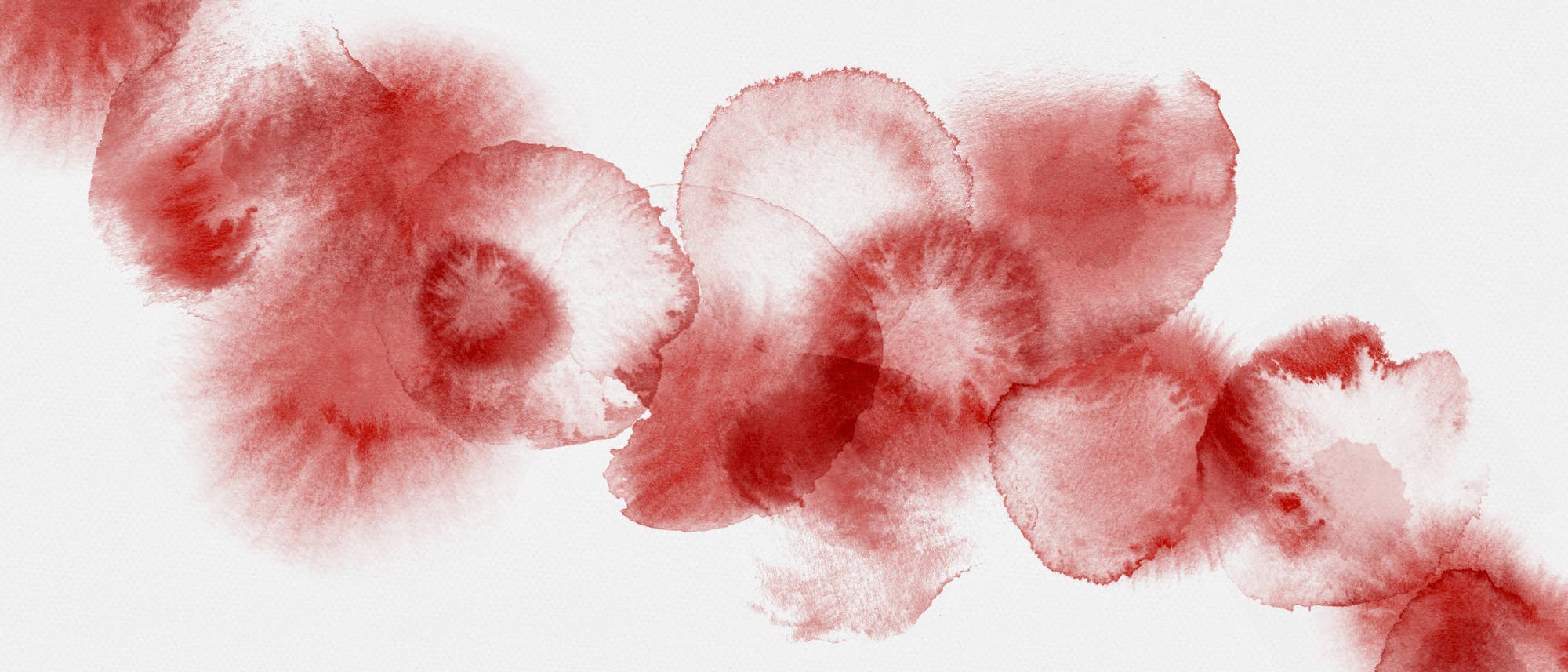 Hellrote Tropfen auf einem hellgrauen Untergrund, die symbolisch für die Menstruationsblutung stehen