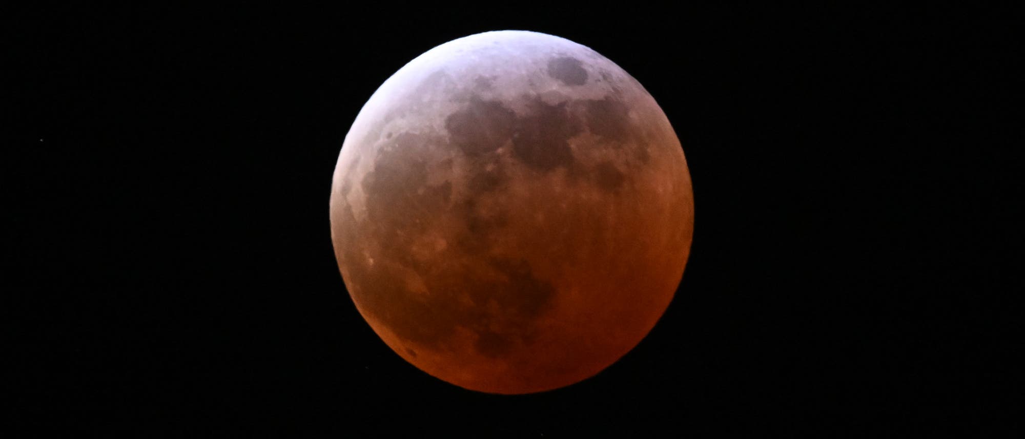 Imagen de un eclipse lunar en el que la luna aparece en tono rojizo. El fondo es un cielo nocturno negro ligero. Imagen de un eclipse lunar en el que la luna aparece en tono rojizo. El fondo es un cielo nocturno negro ligero.