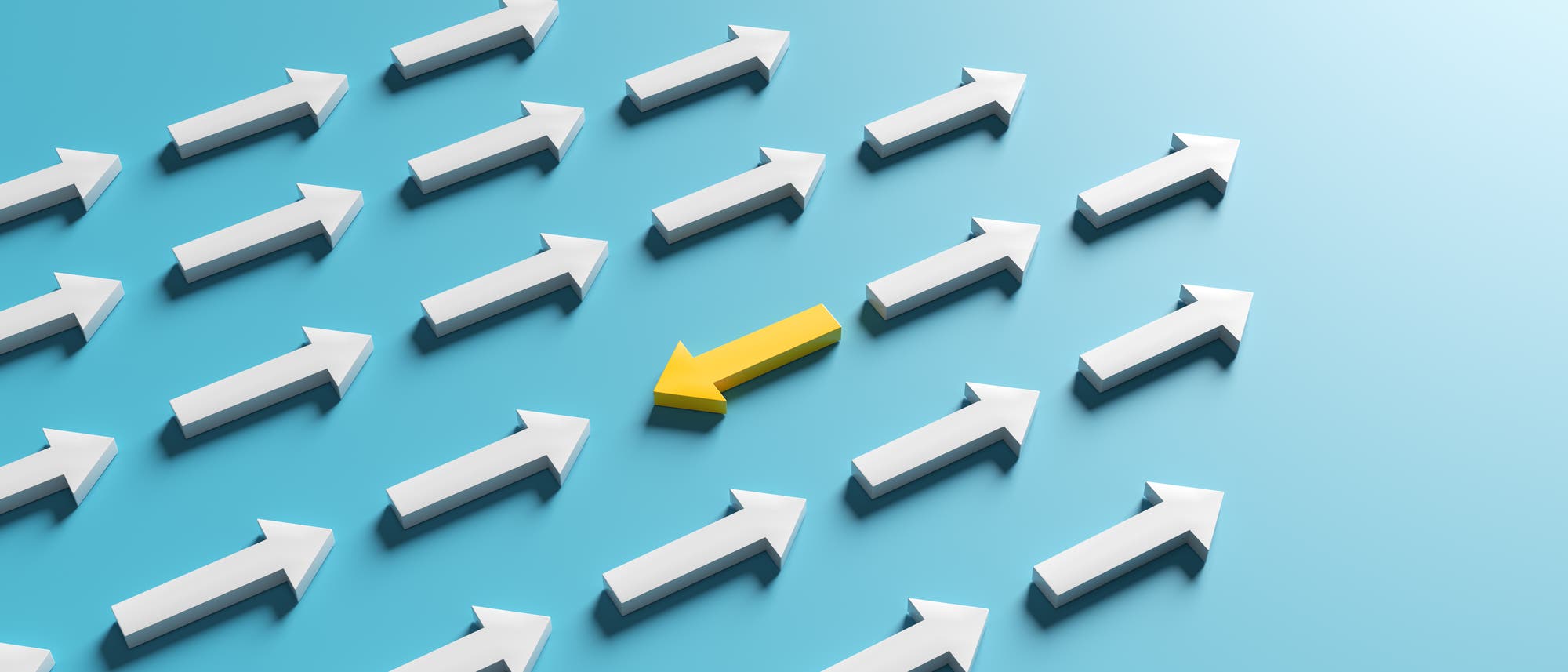 Eine Gruppe weißer Pfeile zeigt nach rechts auf einem blauen Hintergrund. Ein gelber Pfeil in der Mitte zeigt nach links, was symbolisch für Andersdenken oder Individualität steht.