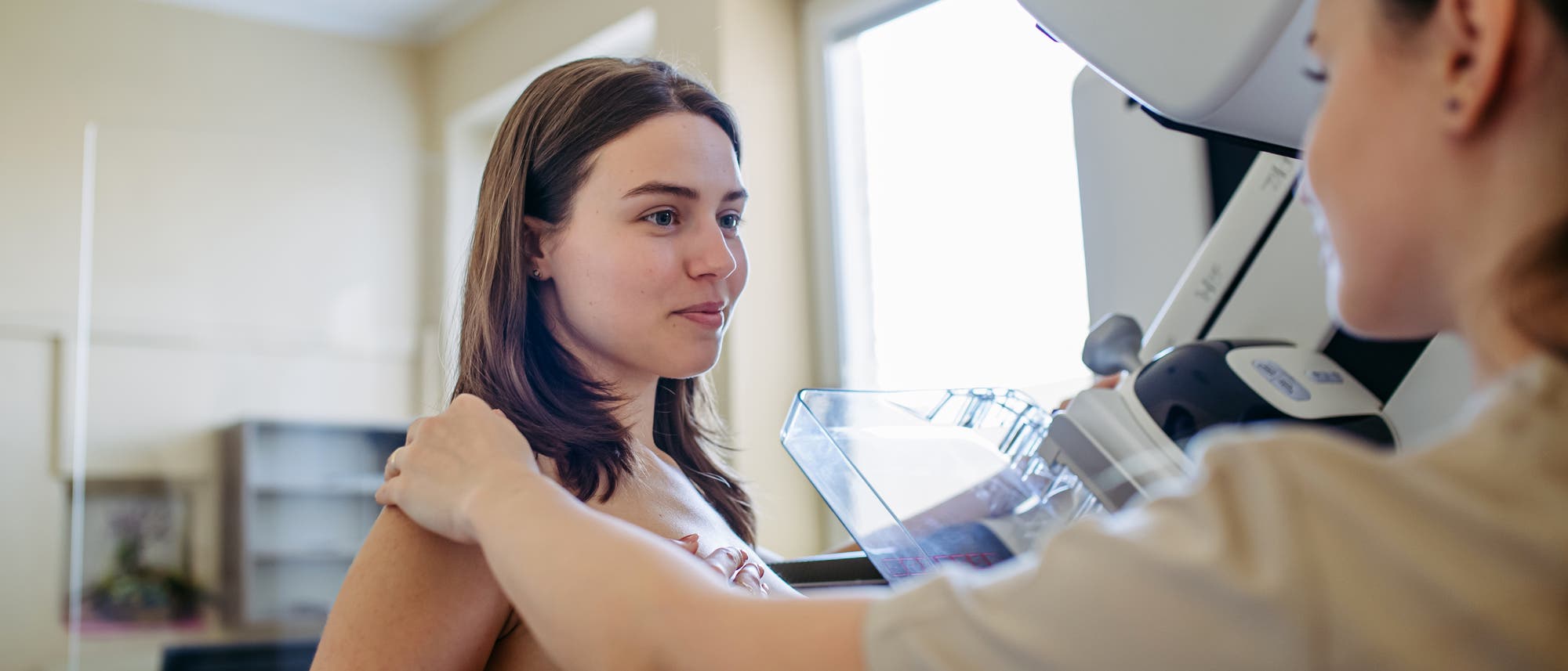 Eine Frau erh&auml;lt eine Mammographie. Eine medizinische Fachkraft legt ihre Hand auf ihre Schulter. 