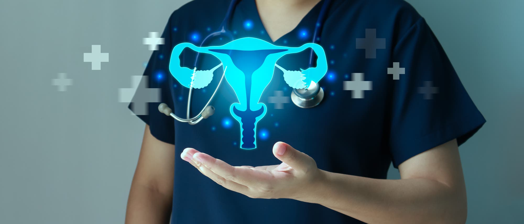 Eine Person in medizinischer Kleidung h&auml;lt ein holografisches Bild eines weiblichen Fortpflanzungssystems, das in leuchtendem Blau dargestellt ist. Das Bild zeigt die Geb&auml;rmutter, die Eileiter und die Eierst&ouml;cke. Im Hintergrund sind medizinische Symbole wie Kreuze zu sehen. Die Person tr&auml;gt eine Maske und ein Stethoskop um den Hals, was auf einen medizinischen Kontext hinweist.