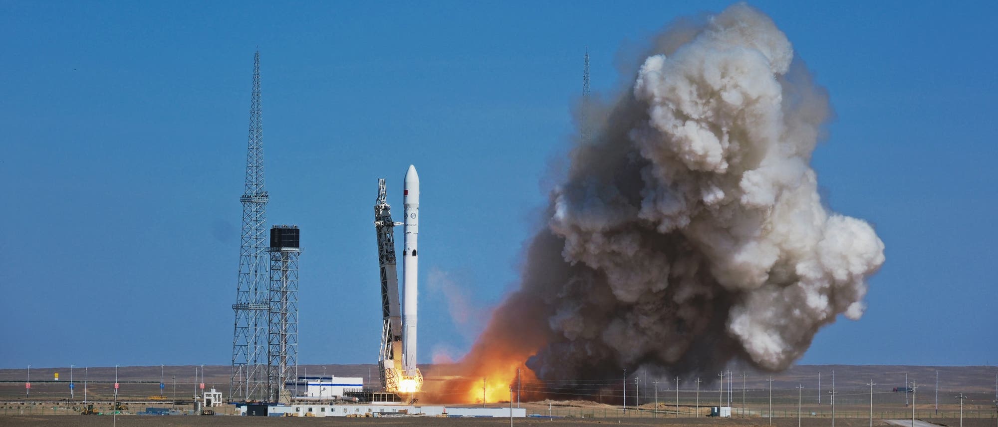 Eine Rakete hebt von einer Startrampe ab, umgeben von dichten Rauchwolken und Flammen. Im Hintergrund sind mehrere hohe Antennen und ein klarer blauer Himmel zu sehen. Die Szene zeigt den Moment des Raketenstarts auf einem offenen Gelände. Eine Rakete hebt von einer Startrampe ab, umgeben von dichten Rauchwolken und Flammen. Im Hintergrund sind mehrere hohe Antennen und ein klarer blauer Himmel zu sehen. Die Szene zeigt den Moment des Raketenstarts auf einem offenen Gelände.