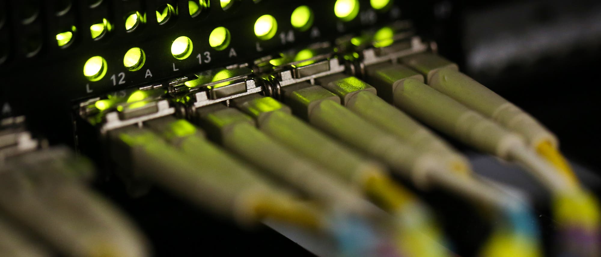 Nahaufnahme eines Netzwerk-Switches mit mehreren eingesteckten Ethernet-Kabeln. Die grünen LED-Anzeigen über den Anschlüssen leuchten, was auf aktive Verbindungen hinweist. Die Anschlüsse sind nummeriert, und die Kabel sind in verschiedenen Farben gehalten. Das Bild vermittelt den Eindruck von Datenverarbeitung und Netzwerktechnologie. Nahaufnahme eines Netzwerk-Switches mit mehreren eingesteckten Ethernet-Kabeln. Die grünen LED-Anzeigen über den Anschlüssen leuchten, was auf aktive Verbindungen hinweist. Die Anschlüsse sind nummeriert, und die Kabel sind in verschiedenen Farben gehalten. Das Bild vermittelt den Eindruck von Datenverarbeitung und Netzwerktechnologie.