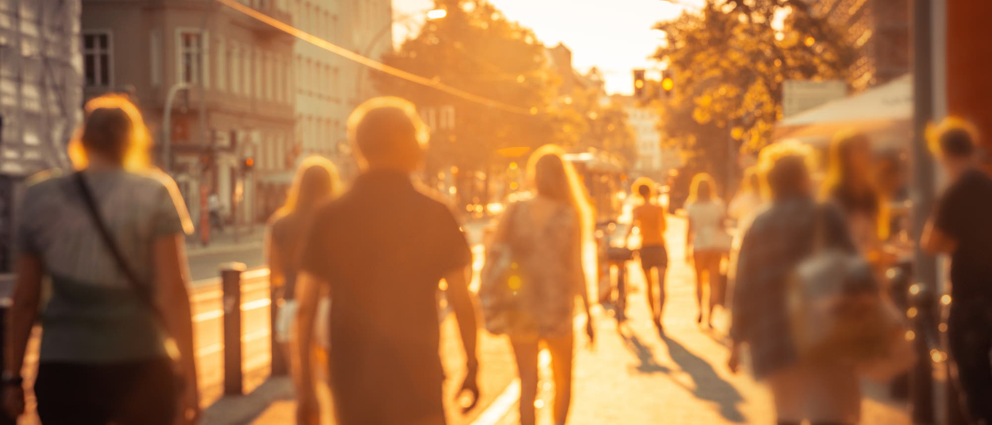 Eine Gruppe von Menschen geht auf einem Bürgersteig in einer Stadt bei starken Sonnenlicht. Eine Gruppe von Menschen geht auf einem Bürgersteig in einer Stadt bei starken Sonnenlicht.