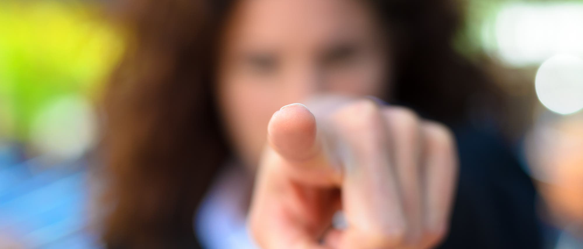 Eine Person zeigt mit dem Finger direkt auf die Kamera. Der Hintergrund ist unscharf, wodurch der Fokus auf der Geste liegt. Die Szene vermittelt den Eindruck von Direktheit oder Aufforderung.