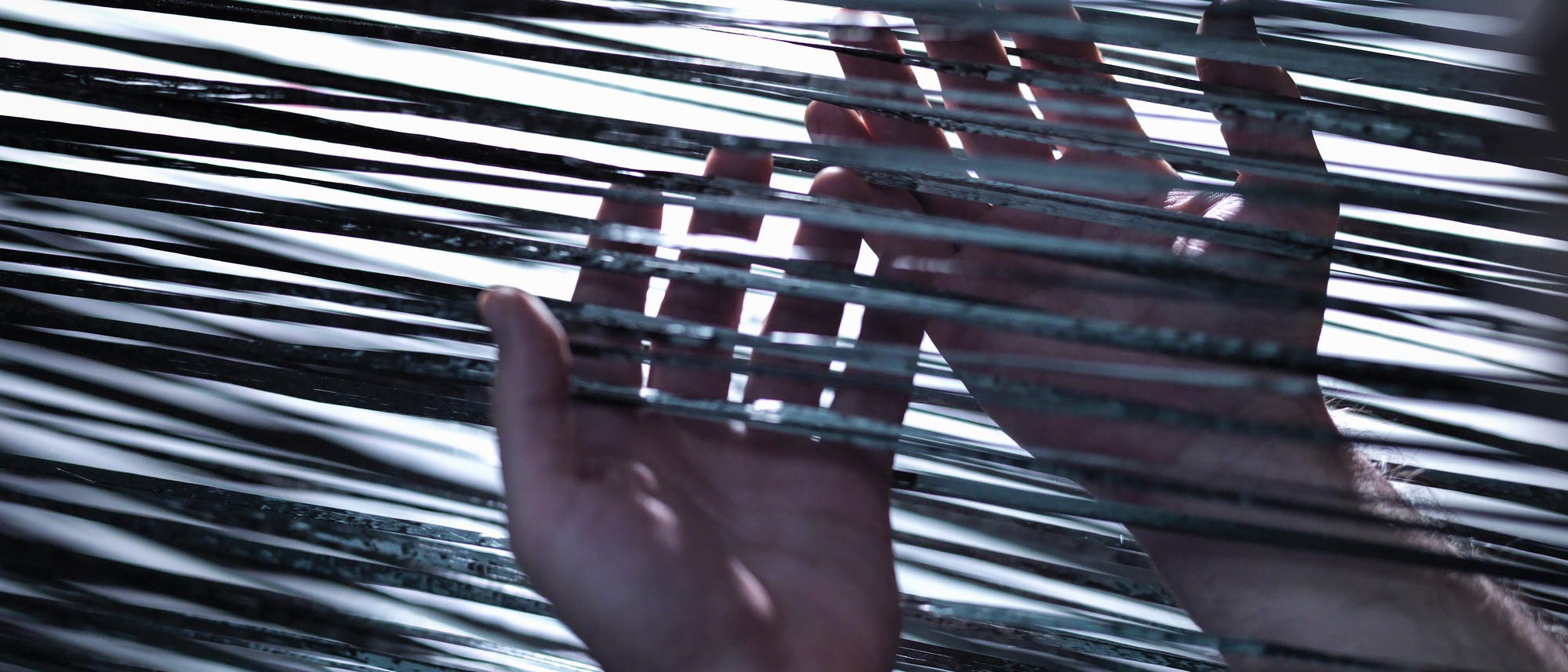 Zwei Hände berühren mehrere parallele, glänzende Fäden oder Drähte, die in horizontalen Linien gespannt sind. Das Licht reflektiert auf den Drähten und erzeugt ein Spiel aus Licht und Schatten. Die Szene vermittelt ein Gefühl von Interaktion und Erkundung.
