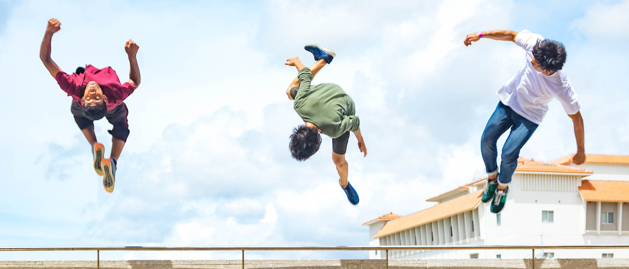 Drei Jugendliche fliegen beim Parkour in städtischer Umgebung durch die Luft.