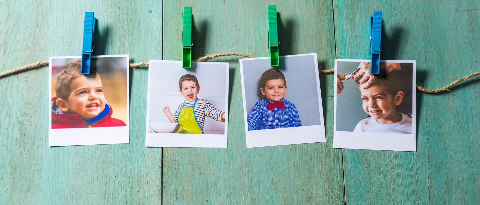 Fotos von vier Kindern sind mit bunten Wäscheklammern an einer Schnur befestigt. Jedes Kind zeigt unterschiedliche Gesichtsausdrücke und Aktivitäten. Der Hintergrund besteht aus einer türkisfarbenen Holzoberfläche. Fotos von vier Kindern sind mit bunten Wäscheklammern an einer Schnur befestigt. Jedes Kind zeigt unterschiedliche Gesichtsausdrücke und Aktivitäten. Der Hintergrund besteht aus einer türkisfarbenen Holzoberfläche.