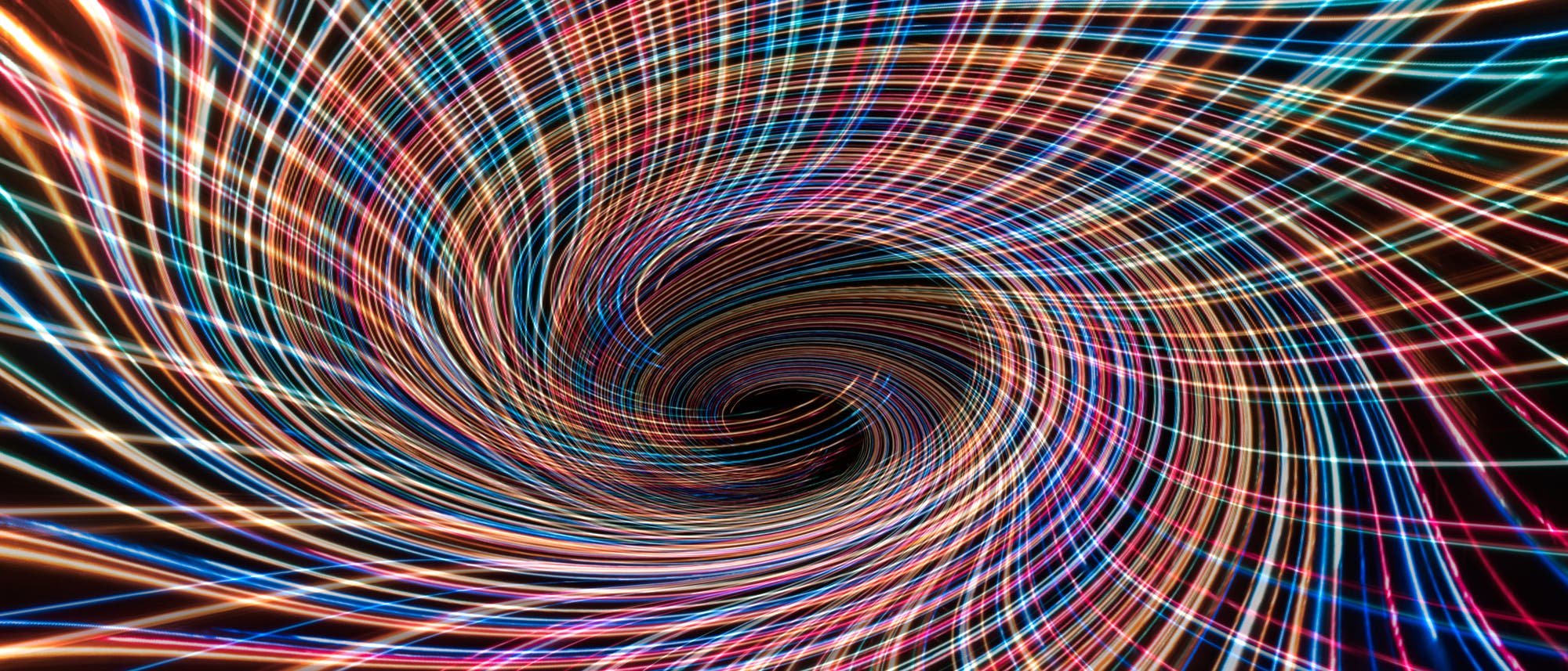 Ein abstraktes Kunstbild zeigt ein spiralf&ouml;rmiges Muster aus leuchtenden, bunten Linien, die sich in einem Wirbel bewegen. Die Linien variieren in Farben wie Blau, Rot, Gelb und Wei&szlig; und erzeugen einen dynamischen, kaleidoskopischen Effekt.