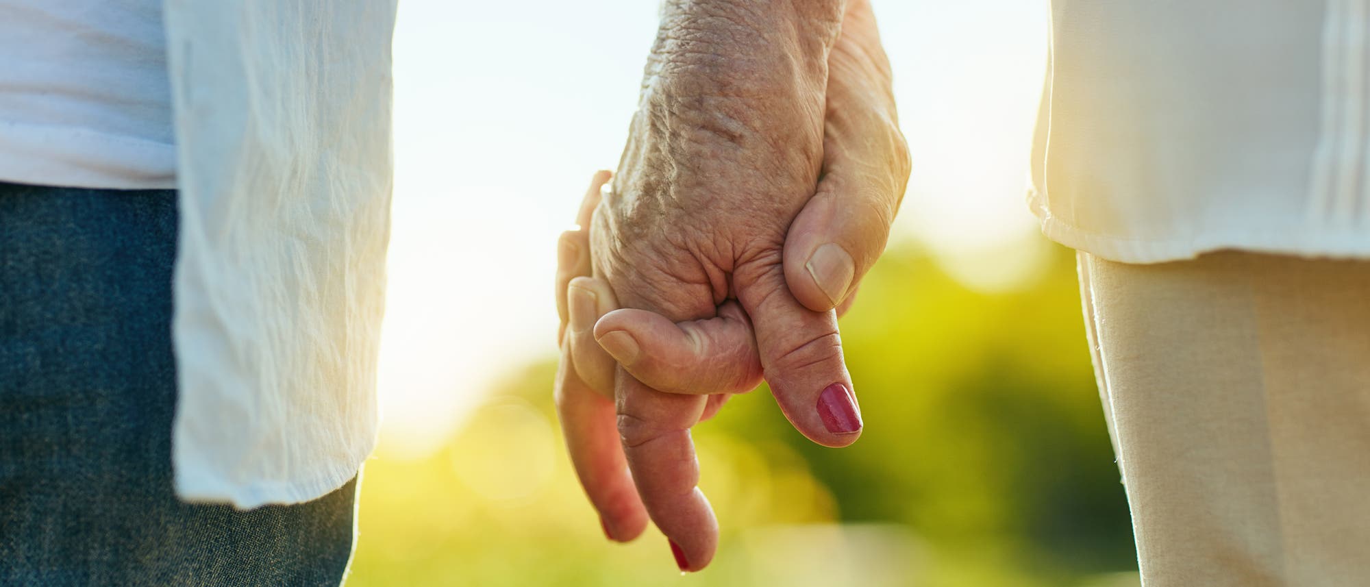 Zwei Personen halten sich an den Händen, während sie im Freien stehen. Die Szene ist in warmes, natürliches Licht getaucht, was eine friedliche und liebevolle Atmosphäre schafft. Eine der Personen trägt Nagellack. Im Hintergrund sind verschwommene grüne Pflanzen zu sehen. Zwei Personen halten sich an den Händen, während sie im Freien stehen. Die Szene ist in warmes, natürliches Licht getaucht, was eine friedliche und liebevolle Atmosphäre schafft. Eine der Personen trägt Nagellack. Im Hintergrund sind verschwommene grüne Pflanzen zu sehen.