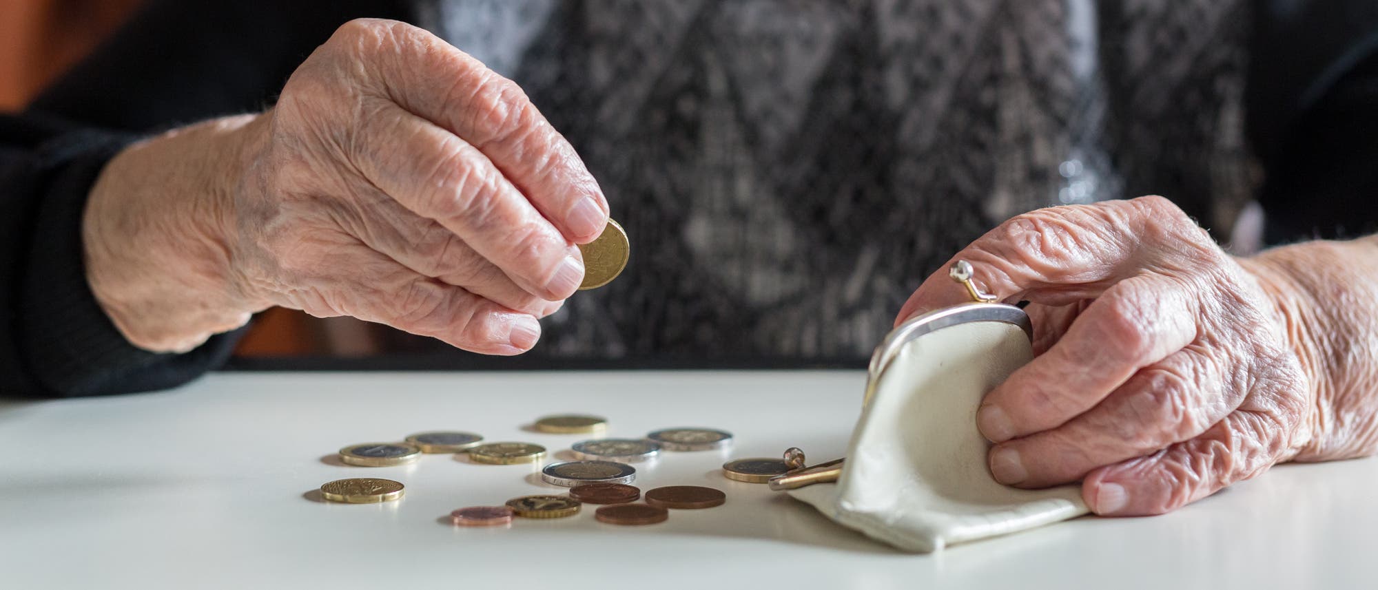 Eine &auml;ltere Frau z&auml;hlt aus ihrer B&ouml;rse ein wenig M&uuml;nzgeld auf den Tisch.