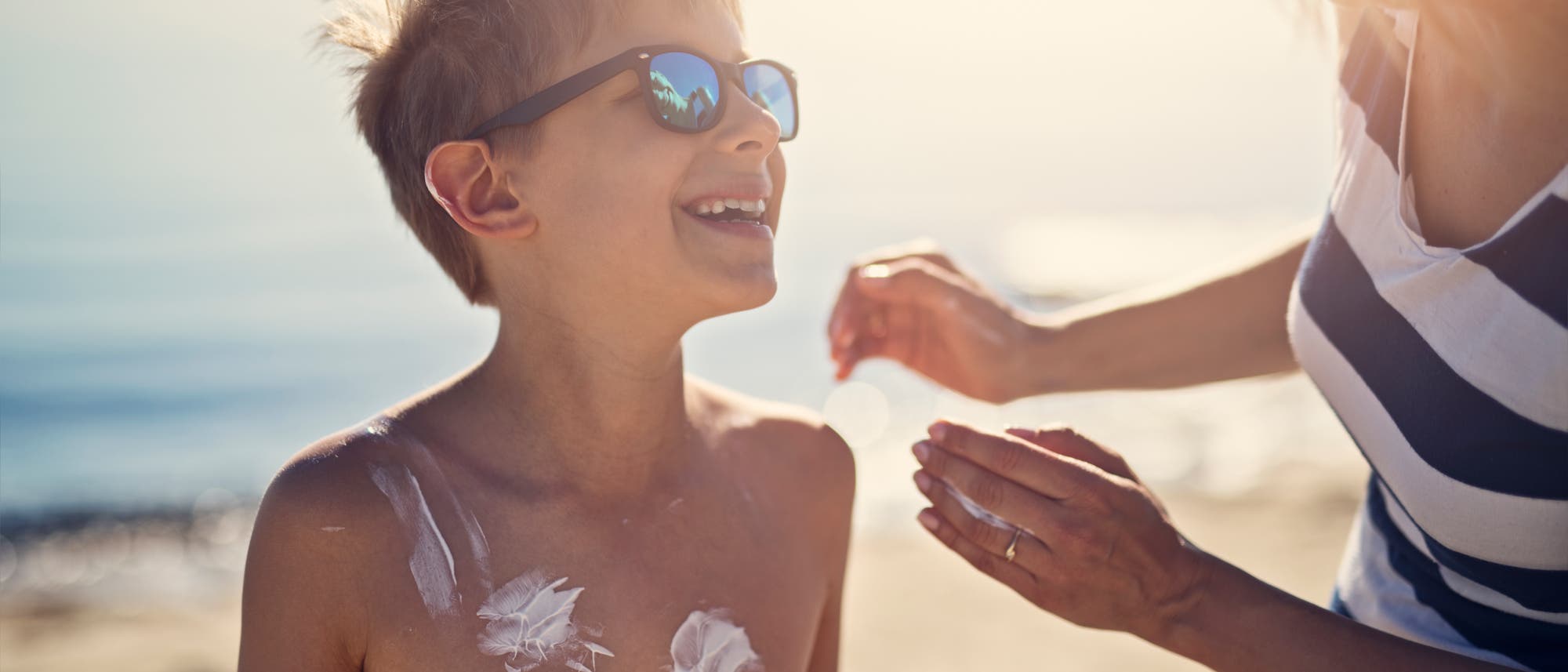 Eine Mutter schmiert ihren Sohn an einem sonnigen Tag am Strand mit Sonnencreme ein.
