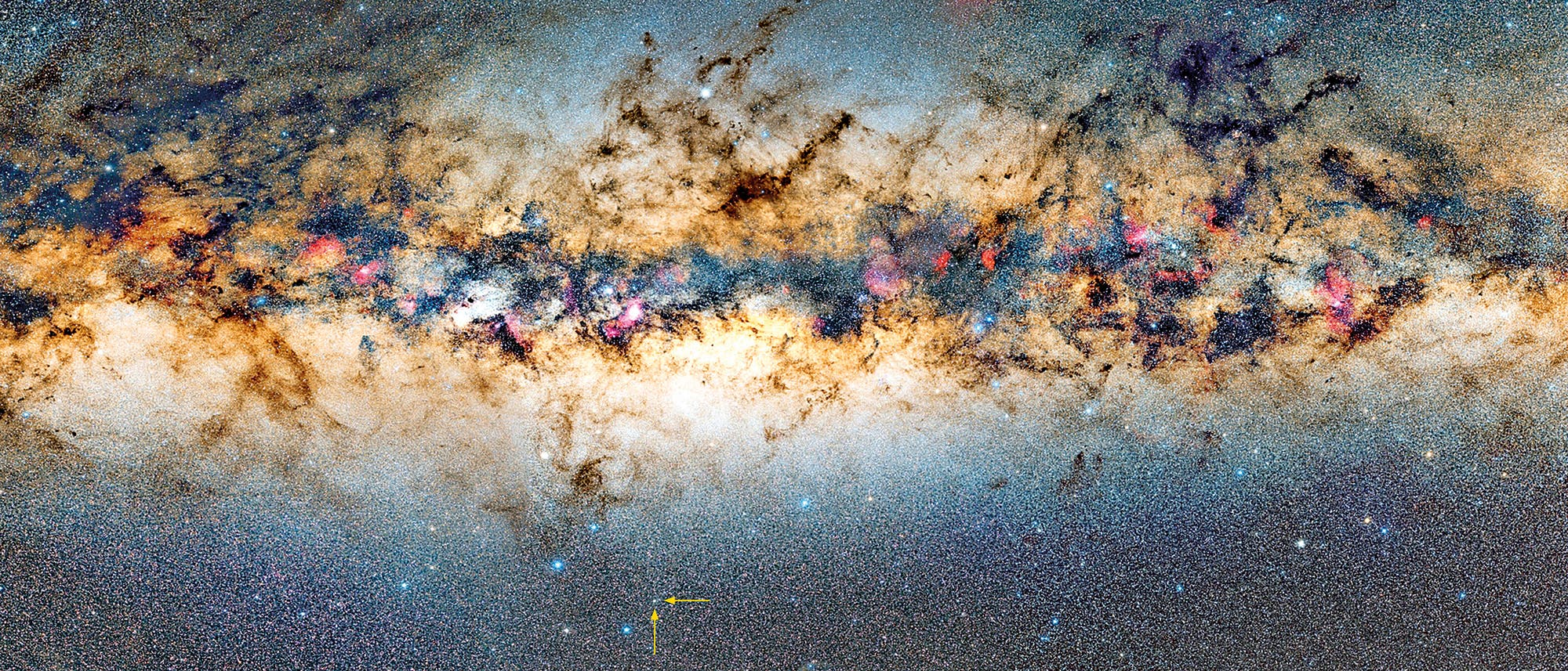 Ein detailliertes Bild der Milchstraße, das den dichten, sternenreichen Streifen der Galaxie zeigt. Dunkle Staubwolken durchziehen das Bild, während bunte Nebel und helle Sterne hervortreten. Ein roter Kreis markiert einen bestimmten Bereich im unteren Teil des Bildes. Die Farben reichen von leuchtendem Blau und Rosa bis zu warmen Gelb- und Brauntönen.