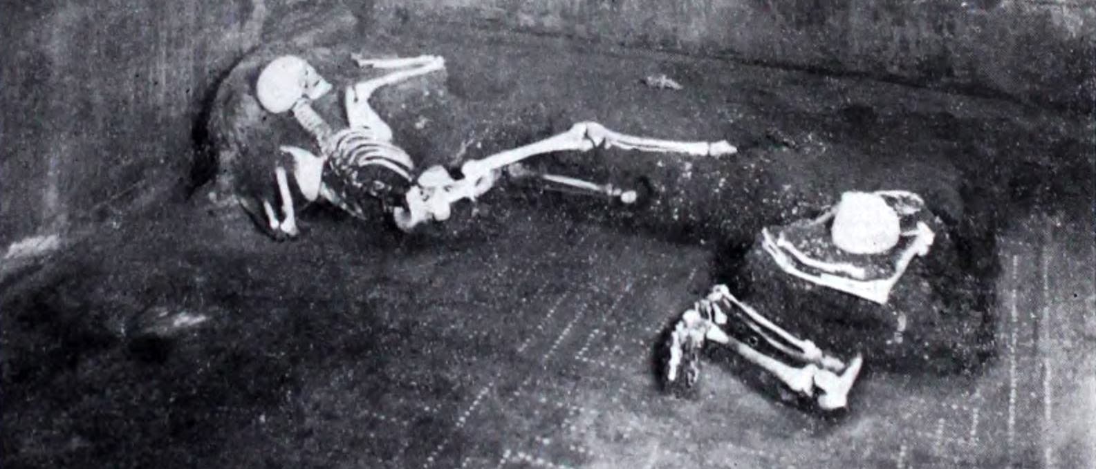 Schwarzweißfoto zweier Skelette vor den Überresten einer Liege.