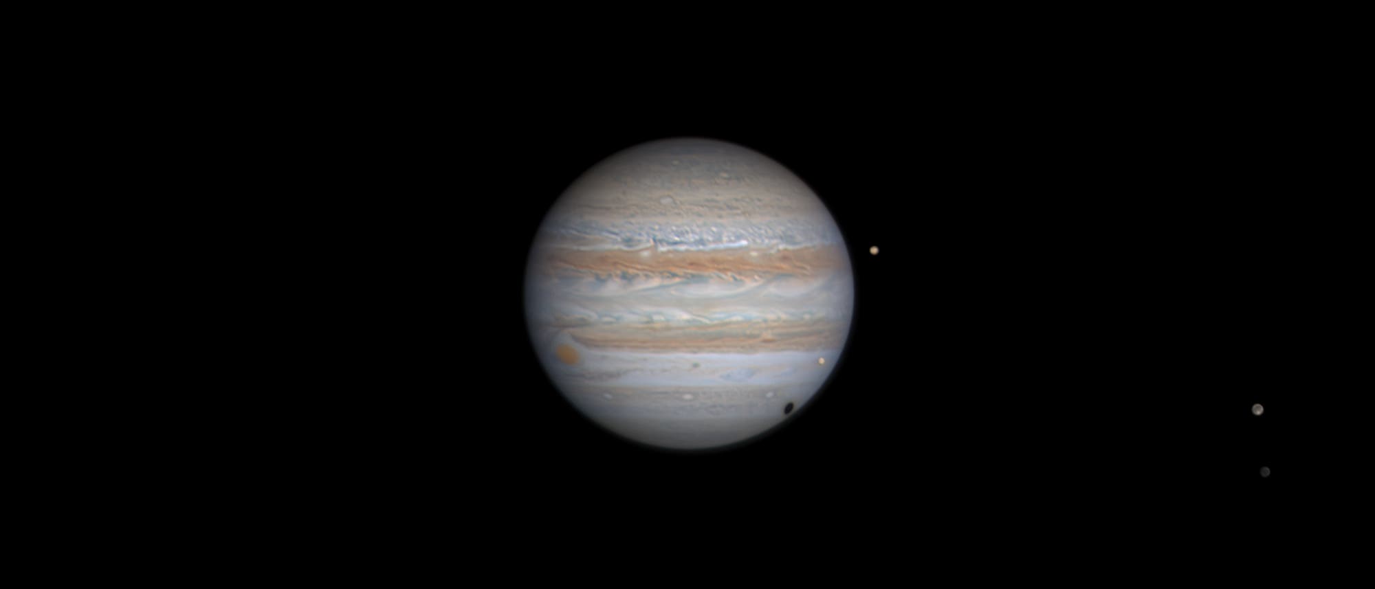 Das Bild zeigt den Planeten Jupiter mit seinen charakteristischen Wolkenbändern in verschiedenen Brauntönen und dem Großen Roten Fleck. Mehrere seiner Monde sind als kleine, helle Punkte sichtbar, die den Planeten umgeben. Der Hintergrund ist schwarz. Das Bild zeigt den Planeten Jupiter mit seinen charakteristischen Wolkenbändern in verschiedenen Brauntönen und dem Großen Roten Fleck. Mehrere seiner Monde sind als kleine, helle Punkte sichtbar, die den Planeten umgeben. Der Hintergrund ist schwarz.