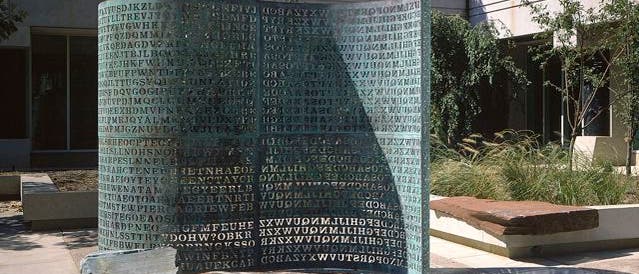 Eine Skulptur im Freien, bestehend aus einer großen, gebogenen Metallplatte mit eingravierten Buchstabenreihen, die wie ein Code oder Rätsel wirken. Die Skulptur steht auf einem Platz vor einem modernen Gebäude mit Glasfenstern. Um die Skulptur herum sind Bäume und Pflanzen zu sehen, die eine harmonische Verbindung zwischen Kunst und Natur schaffen. Die Buchstaben werfen Schatten auf den Boden, was dem Kunstwerk eine zusätzliche Dimension verleiht. Eine Skulptur im Freien, bestehend aus einer großen, gebogenen Metallplatte mit eingravierten Buchstabenreihen, die wie ein Code oder Rätsel wirken. Die Skulptur steht auf einem Platz vor einem modernen Gebäude mit Glasfenstern. Um die Skulptur herum sind Bäume und Pflanzen zu sehen, die eine harmonische Verbindung zwischen Kunst und Natur schaffen. Die Buchstaben werfen Schatten auf den Boden, was dem Kunstwerk eine zusätzliche Dimension verleiht.