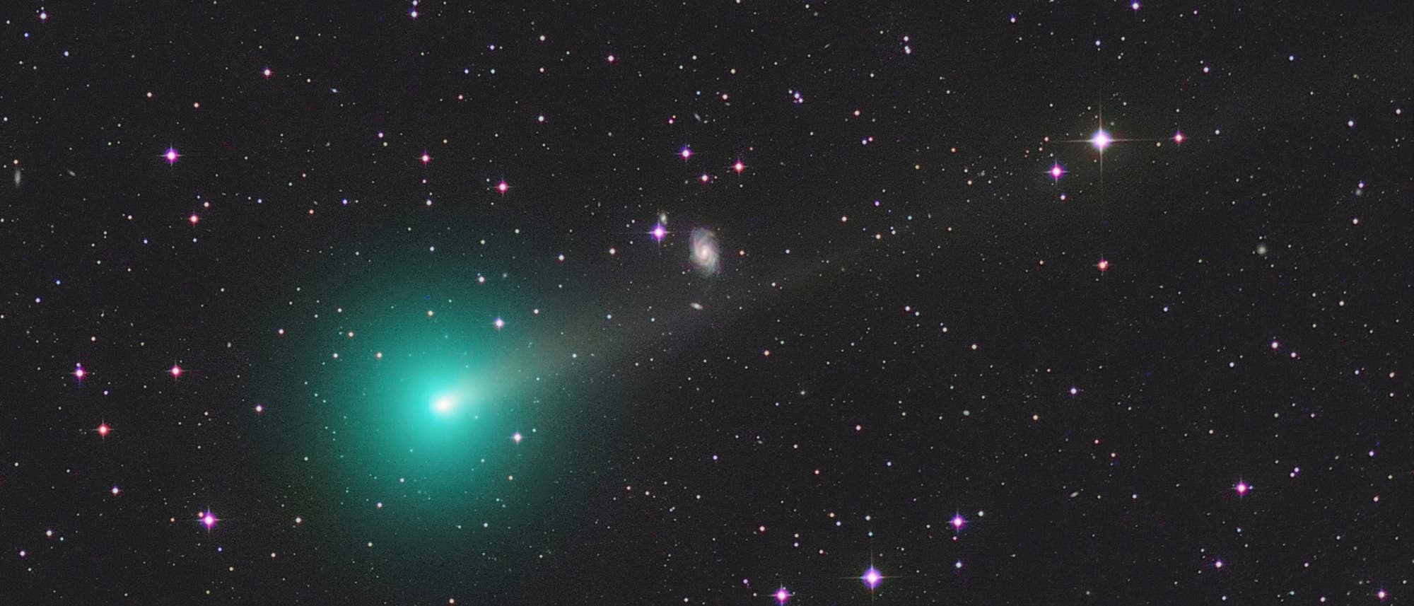 Ein leuchtend grüner Komet mit einem langen Schweif zieht durch ein Sternenfeld im Weltraum. Der Komet ist links im Bild prominent sichtbar, während zahlreiche Sterne unterschiedlicher Helligkeit den Hintergrund füllen. Einige Galaxien sind ebenfalls erkennbar. Das Bild zeigt die Schönheit und Weite des Universums. Ein leuchtend grüner Komet mit einem langen Schweif zieht durch ein Sternenfeld im Weltraum. Der Komet ist links im Bild prominent sichtbar, während zahlreiche Sterne unterschiedlicher Helligkeit den Hintergrund füllen. Einige Galaxien sind ebenfalls erkennbar. Das Bild zeigt die Schönheit und Weite des Universums.