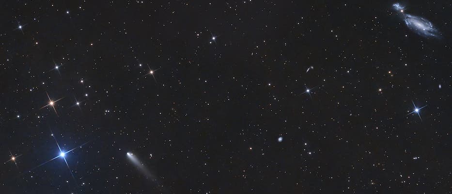 Ein astronomisches Bild zeigt einen Sternenhimmel mit zahlreichen leuchtenden Sternen unterschiedlicher Helligkeit. In der Mitte des Bildes ist ein Komet mit einem deutlich sichtbaren Schweif zu erkennen. Oben rechts befindet sich eine Galaxie mit spiralf&ouml;rmigen Strukturen. Der Hintergrund ist dunkel, was die Helligkeit der Sterne und des Kometen betont. Das Bild vermittelt die Weite und Sch&ouml;nheit des Universums.