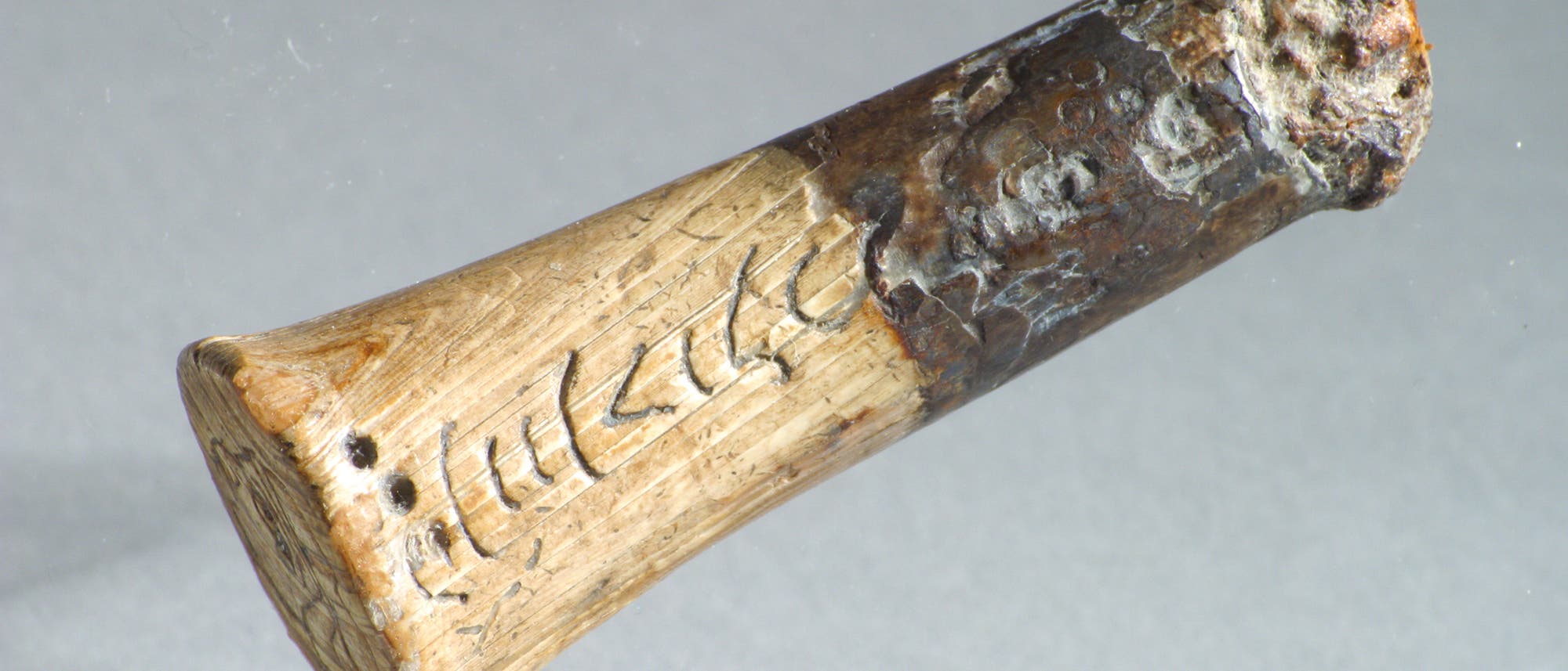 Im Bild zu sehen ist ein antiker Messergriff aus Elfenbein, in dem altindische Schriftzeichen eingeritzt sind. 