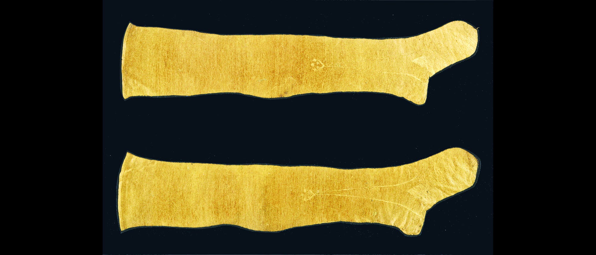 Ein Paar goldgl&auml;nzende Str&uuml;mpfe aus Muschelseide, gewebt aus den Byssusf&auml;den der 'Edlen Steckmuschel' auf schwarzem Hintergrund. 