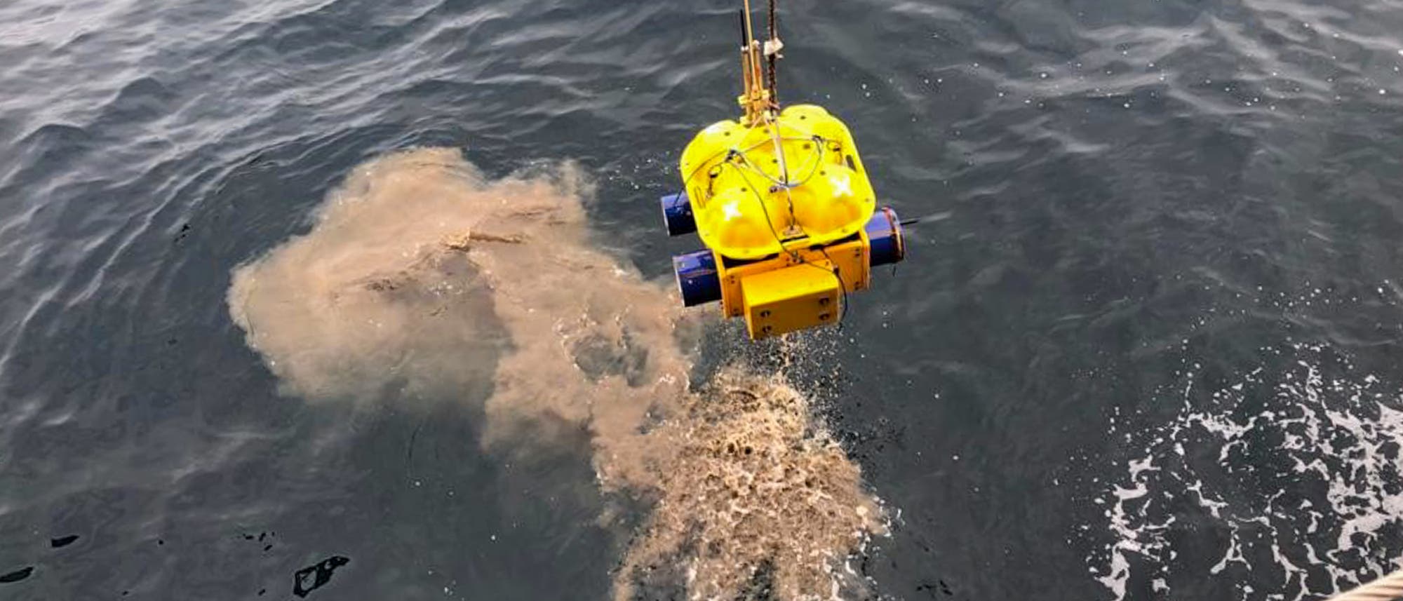 Ein gelbes Ozeanbodenseismometer mit blauen Propellern wird mit einem Seil aus dem Meer gezogen. Ein orangefarbenes Fähnchen ist am Fahrzeug befestigt. Im Wasser darunter ist eine aufgewirbelte Sedimentwolke zu sehen. Das Bild zeigt den Einsatz eines ferngesteuerten Tauchroboters zur Untersuchung des Meeresbodens. Ein gelbes Ozeanbodenseismometer mit blauen Propellern wird mit einem Seil aus dem Meer gezogen. Ein orangefarbenes Fähnchen ist am Fahrzeug befestigt. Im Wasser darunter ist eine aufgewirbelte Sedimentwolke zu sehen. Das Bild zeigt den Einsatz eines ferngesteuerten Tauchroboters zur Untersuchung des Meeresbodens.