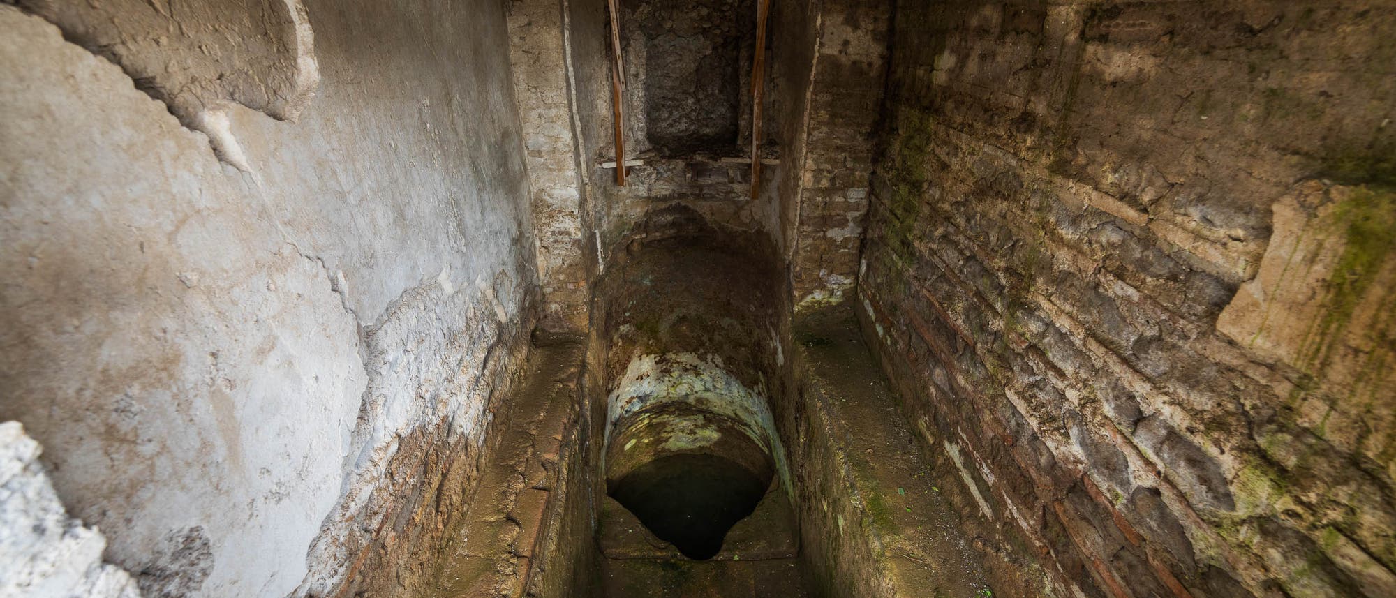 Ein alter, schmaler Tunnel mit abgenutzten Steinwänden und einer Holzabdeckung oben. Der Boden ist feucht und moosbewachsen, was auf eine lange Vernachlässigung hindeutet. Der Tunnel führt in die Dunkelheit, was eine geheimnisvolle und historische Atmosphäre erzeugt. Ein alter, schmaler Tunnel mit abgenutzten Steinwänden und einer Holzabdeckung oben. Der Boden ist feucht und moosbewachsen, was auf eine lange Vernachlässigung hindeutet. Der Tunnel führt in die Dunkelheit, was eine geheimnisvolle und historische Atmosphäre erzeugt.