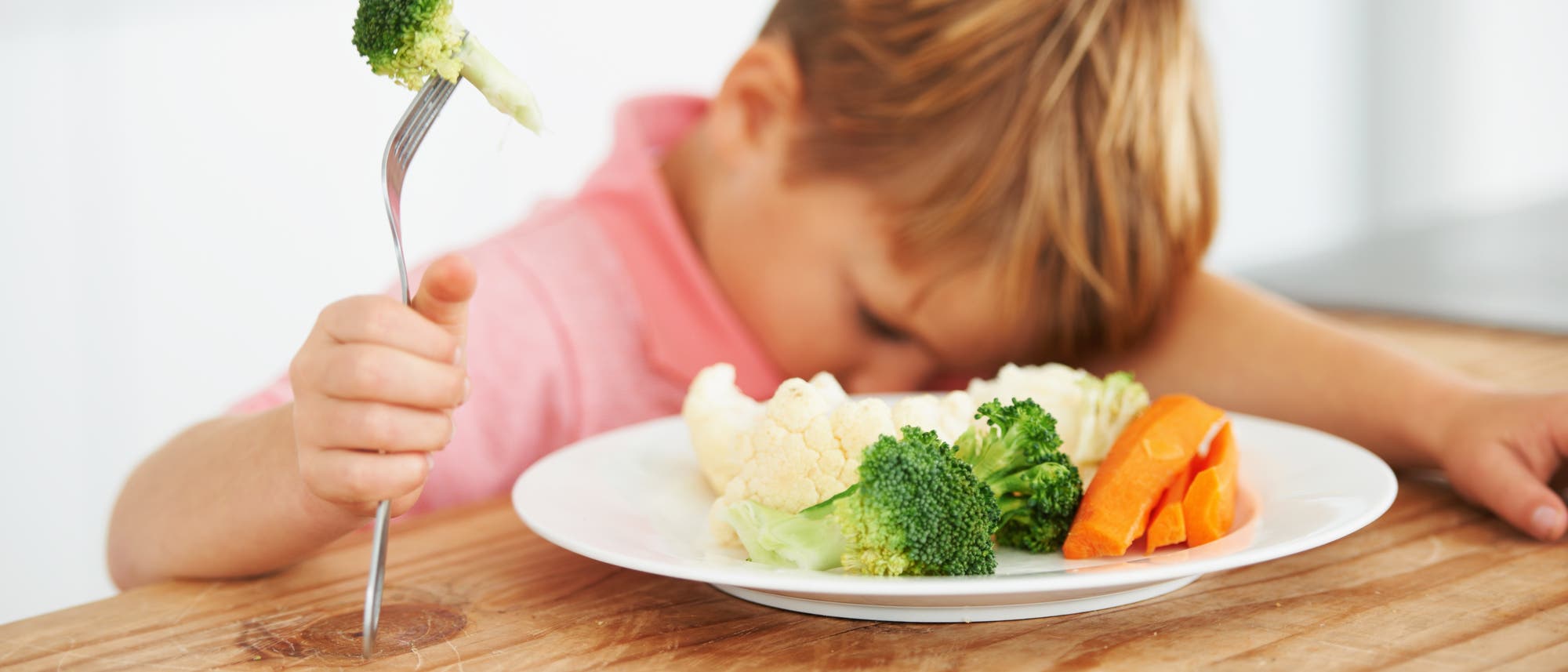 Kind vor einem Teller Gemüse mit einer Gabel in der Hand 