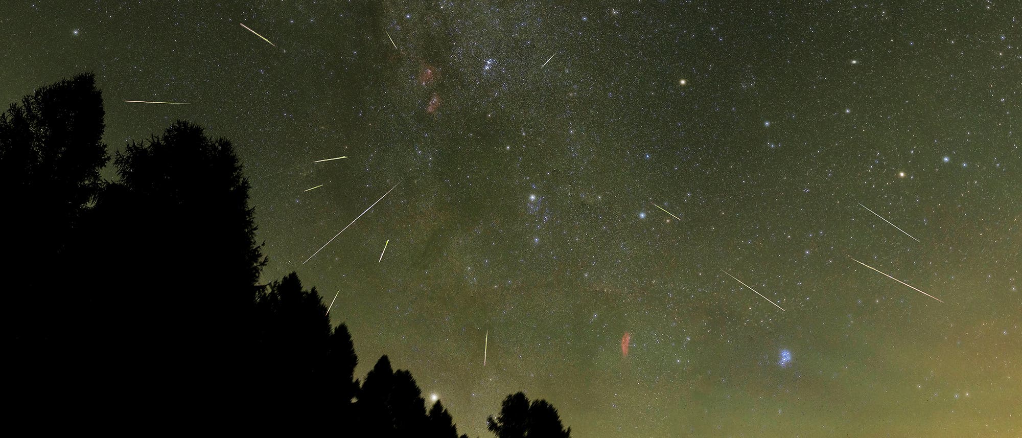 Eine nächtliche Himmelsaufnahme zeigt einen Sternenhimmel mit zahlreichen Sternschnuppen, die in verschiedenen Richtungen über den Himmel ziehen. Im Vordergrund sind die Silhouetten von Bäumen zu sehen. Der Himmel ist mit unzähligen Sternen übersät, und die Milchstraße ist deutlich erkennbar. Die Szene vermittelt den Eindruck eines klaren, ungestörten Blicks auf das Universum. Eine nächtliche Himmelsaufnahme zeigt einen Sternenhimmel mit zahlreichen Sternschnuppen, die in verschiedenen Richtungen über den Himmel ziehen. Im Vordergrund sind die Silhouetten von Bäumen zu sehen. Der Himmel ist mit unzähligen Sternen übersät, und die Milchstraße ist deutlich erkennbar. Die Szene vermittelt den Eindruck eines klaren, ungestörten Blicks auf das Universum.