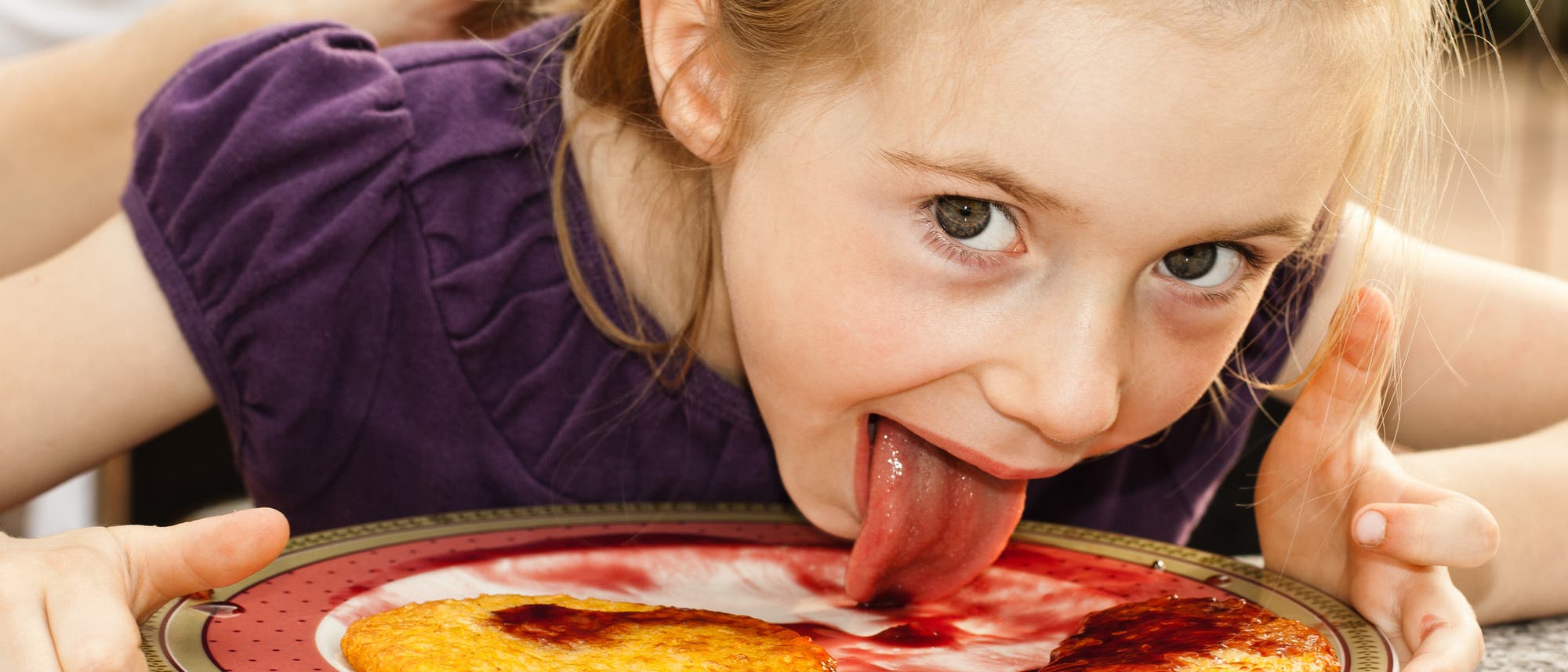 Kind schleckt Teller mit Pfannkuchen und Erdbeersoße