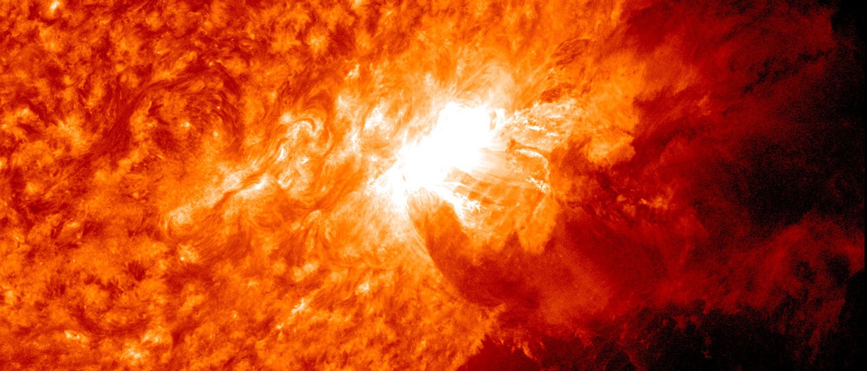 Eine Nahaufnahme der Sonne zeigt einen intensiven Sonnenausbruch, der als heller, leuchtender Bereich auf der Oberfläche sichtbar ist. Die umgebende Sonnenoberfläche ist in verschiedenen Orangetönen dargestellt, die die Textur und Aktivität der Sonnenkorona hervorheben. Der Ausbruch erzeugt eine auffällige Struktur aus Plasma, das sich von der Sonnenoberfläche wegbewegt. Dieses astronomische Bild veranschaulicht die Dynamik und Energie der Sonnenaktivität.