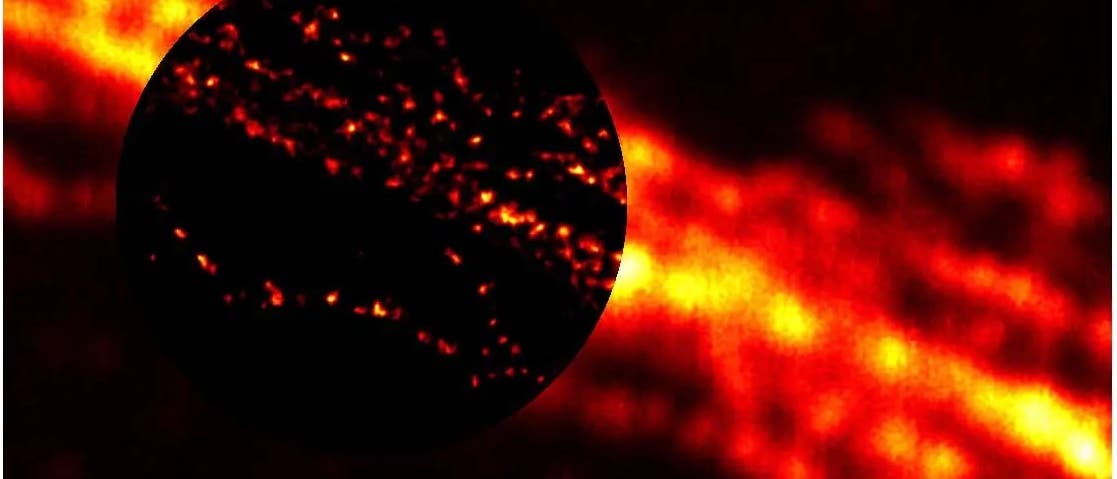 Ein fluoreszenzmikroskopisches Bild zeigt eine leuchtende, fadenförmige Struktur in Rot- und Gelbtönen. Ein vergrößerter kreisförmiger Ausschnitt hebt detaillierte, punktförmige Fluoreszenzsignale hervor, die entlang der Struktur verteilt sind. Das Bild veranschaulicht die Verteilung fluoreszierender Moleküle in einer biologischen Probe. Ein fluoreszenzmikroskopisches Bild zeigt eine leuchtende, fadenförmige Struktur in Rot- und Gelbtönen. Ein vergrößerter kreisförmiger Ausschnitt hebt detaillierte, punktförmige Fluoreszenzsignale hervor, die entlang der Struktur verteilt sind. Das Bild veranschaulicht die Verteilung fluoreszierender Moleküle in einer biologischen Probe.