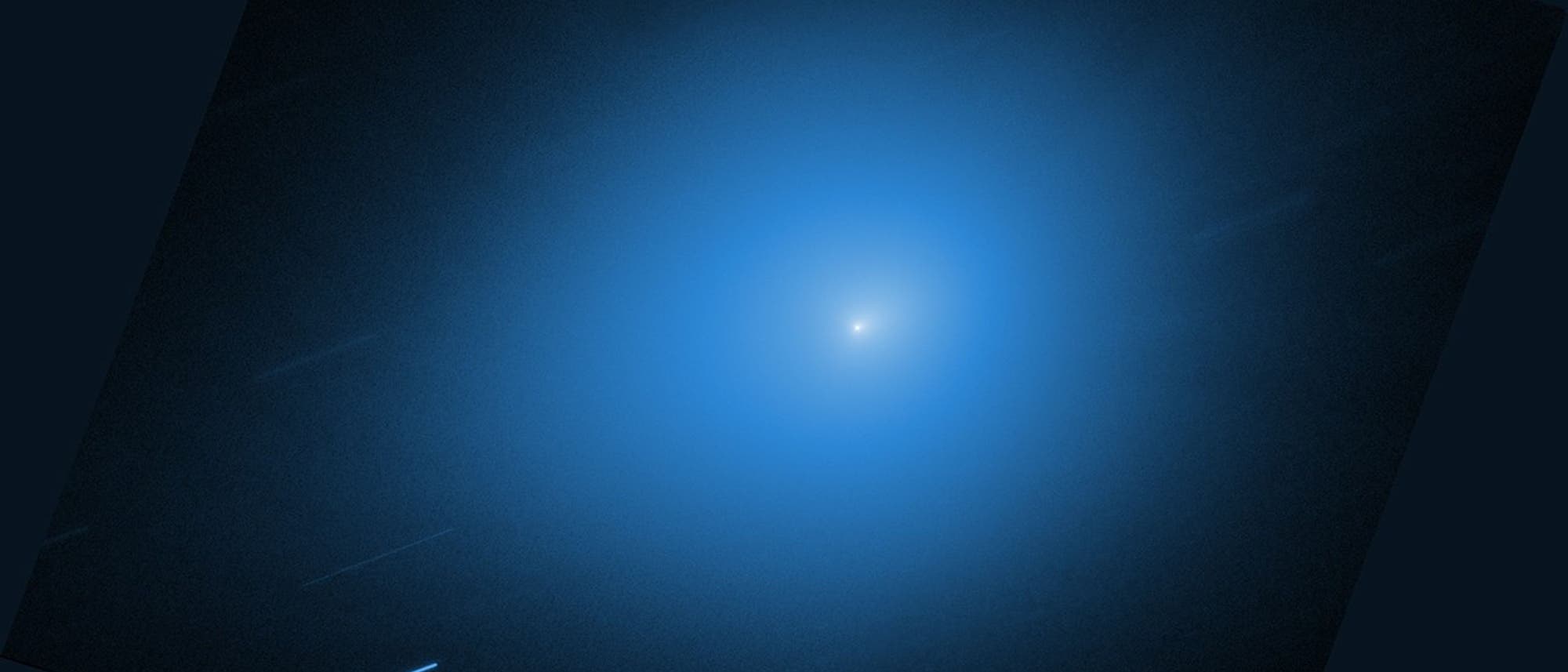 Ein astronomisches Bild zeigt einen Kometen mit einem hellen Kern, umgeben von einer diffusen, blauen Koma. Der Hintergrund ist dunkel, was den Kontrast zur leuchtenden Koma verst&auml;rkt. Mehrere schwache, diagonale Linien deuten auf Sterne oder andere Himmelsk&ouml;rper hin, die w&auml;hrend der Belichtungszeit erfasst wurden. Das Bild vermittelt den Eindruck von Bewegung und Tiefe im Weltraum.