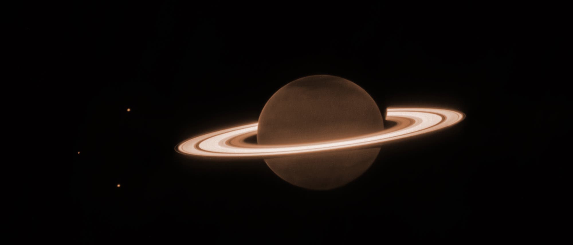 Der Gasplanet Saturn ist orangefarben dargestellt. Gut erkennbar sind seine auffälliges Ringsystem mit Strefen sowie drei seiner Monde links von der Planetenkugel. Der Gasplanet Saturn ist orangefarben dargestellt. Gut erkennbar sind seine auffälliges Ringsystem mit Strefen sowie drei seiner Monde links von der Planetenkugel.