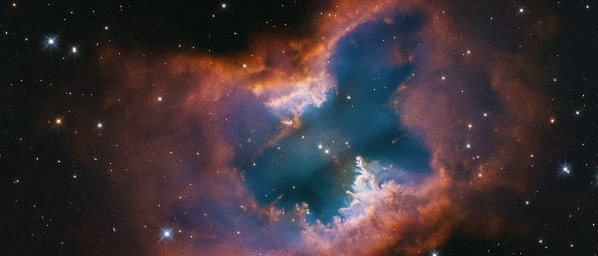 Ein atemberaubendes Bild des Weltraums zeigt den NGC 2899-Nebel, der wie ein Schmetterling geformt ist. Die leuchtenden Farben reichen von tiefem Blau im Zentrum bis zu leuchtendem Orange an den R&auml;ndern, umgeben von einem dunklen Sternenhintergrund. Zahlreiche kleine Sterne sind im gesamten Bild sichtbar. Dieses Bild vermittelt die Sch&ouml;nheit und Komplexit&auml;t des Universums.